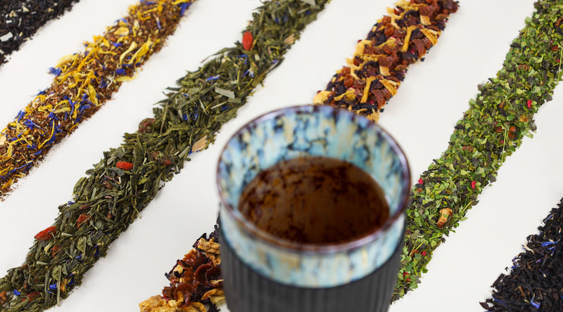 Ceramic Mug with various loose leaf teas behind it
