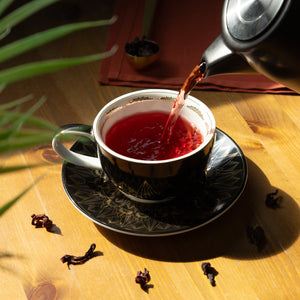 Pouring brewed Hibiscus into a Black & Gold Cup & Saucer.
