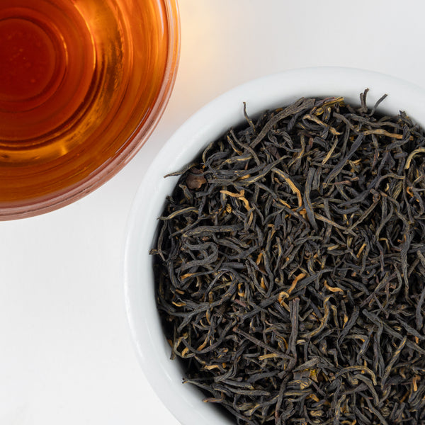 A topdown view of loose leaf tea next to a cup of brewed tea