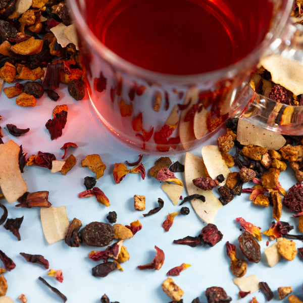Glass of Raspberry Cherry Compote tea next to Raspberry Cherry Compote tea leaves.