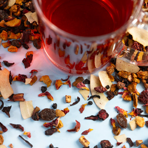 Glass of Raspberry Cherry Compote tea next to Raspberry Cherry Compote tea leaves. 