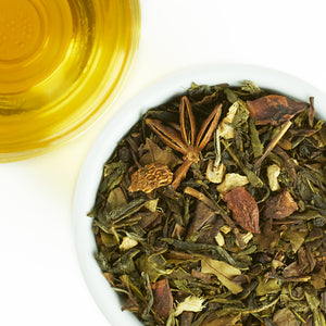 Tea leaves in a bowl with a glass of tea on a white background