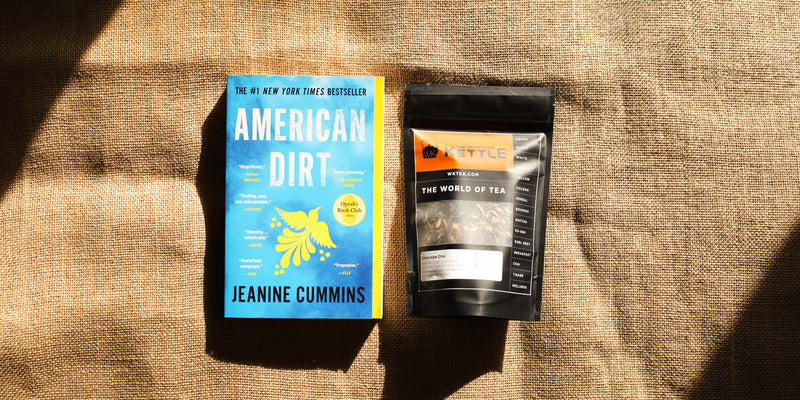 A paperback copy of American Dirt by Jeanine Cummins sits next to a bag of Chocolate Chai tea from The Whistling Kettle