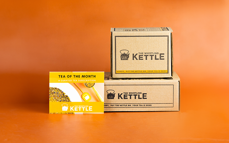Two The Whistling Kettle Tea of the Month gift boxes sit on an orange background