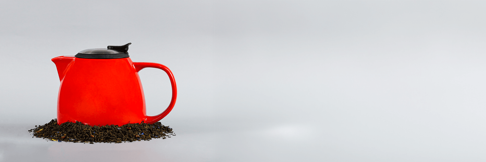 A red tea pot on a bed of tea leaves