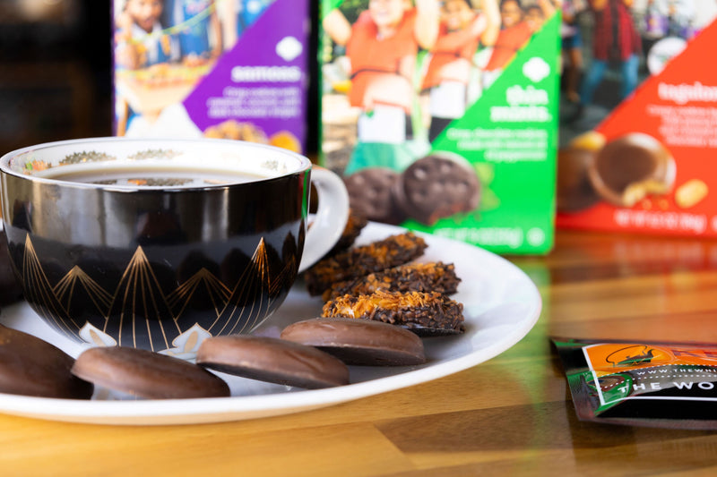 Assorted girl scout cookies on a plate with a cup of tea
