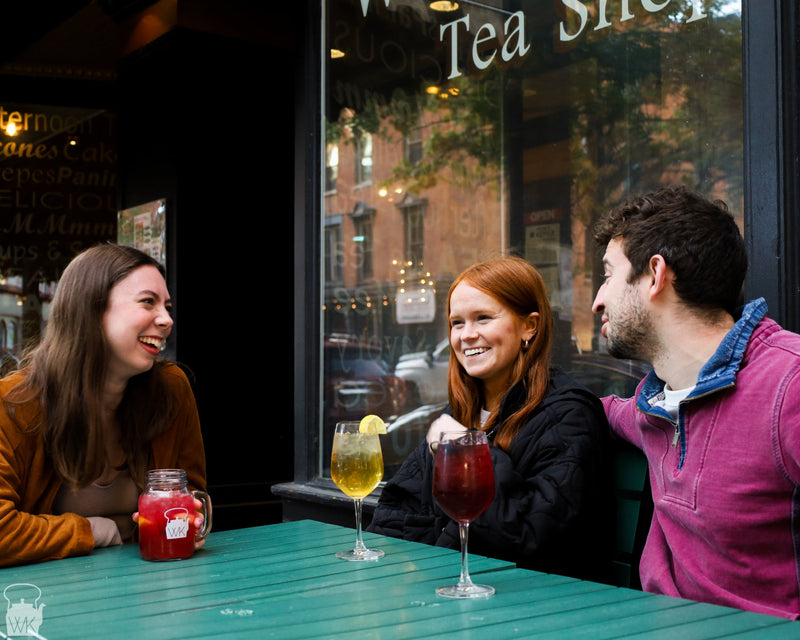 Three friends talk over colorful drinks at an outdoor tea shop