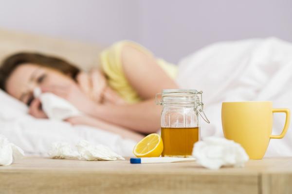 A woman laying in bed sick with lemon tea next to her.