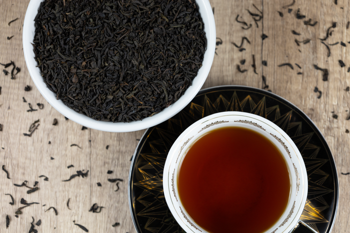 A cup of brewed Lapsang Souchong sits next to a bowl of loose tea leaves