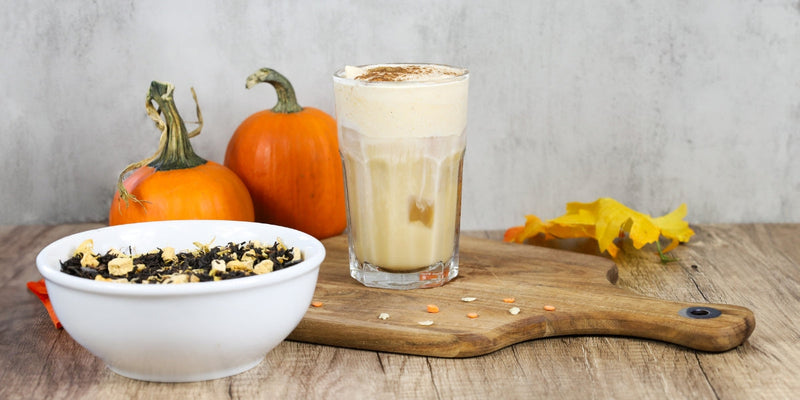 Iced Pumpkin Chai Latte on a brown cutting board, next to small pumpkins and loose leaf Pumpkin Chai tea