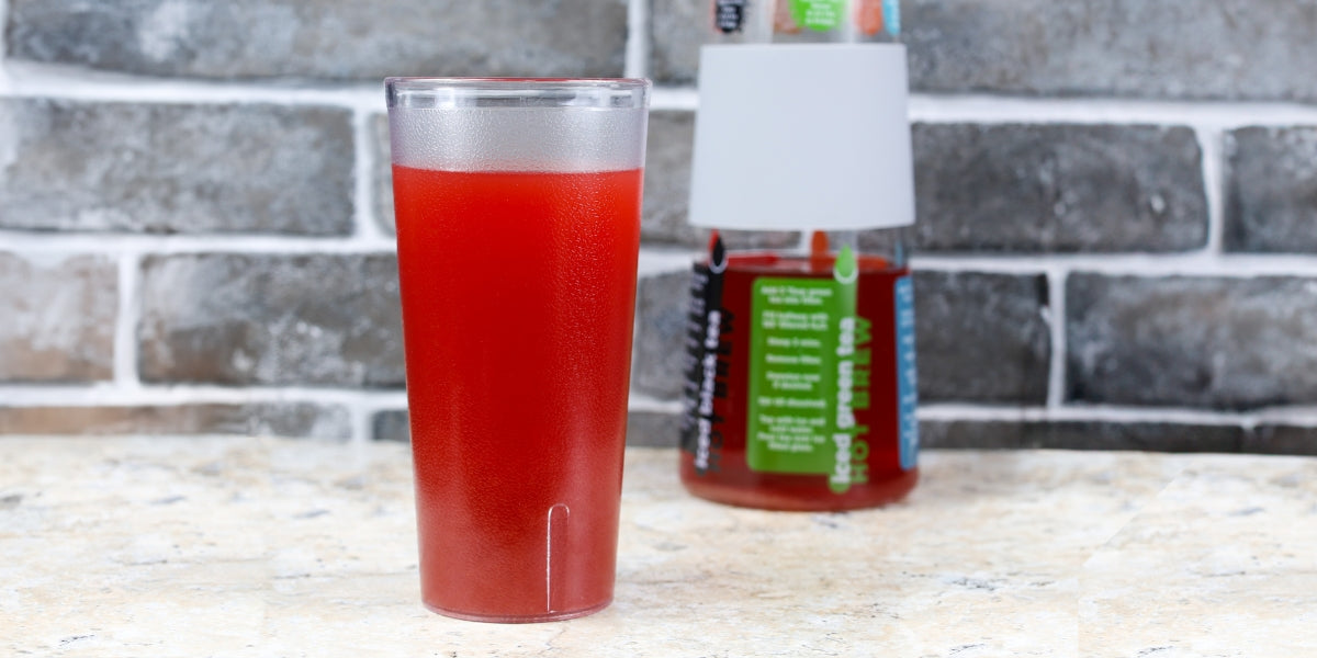 Strawberry Guava sports drink in a plastic cup with a whistling kettle iced tea brewer behind