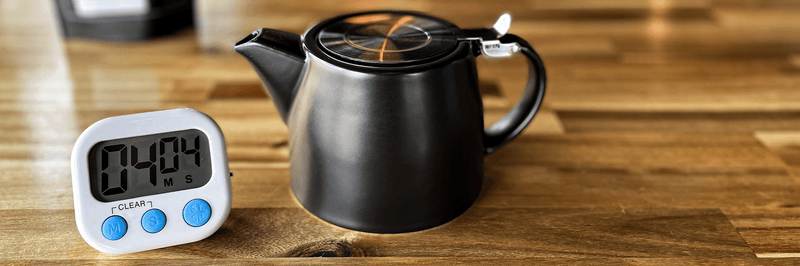 A tea timer next to a tea pot.