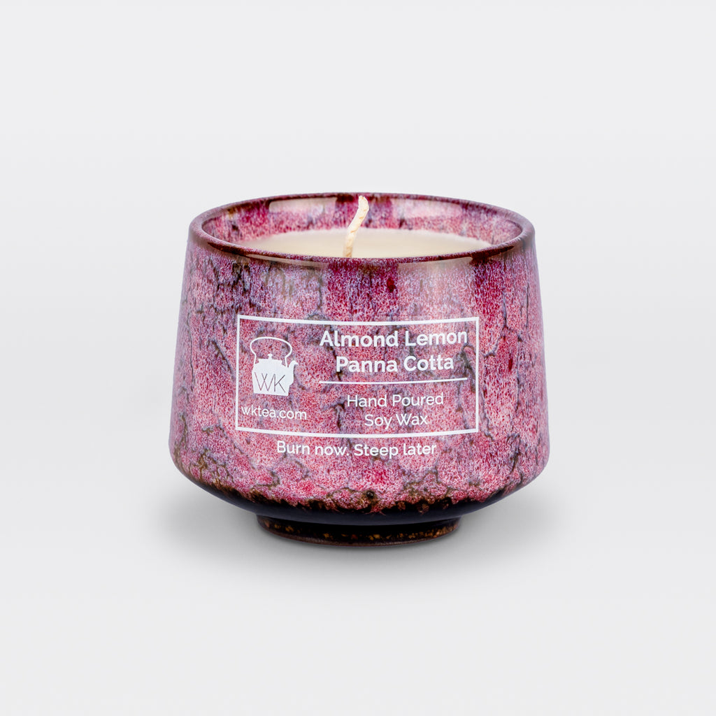 A  candle and wick inside a handmade pink and black marbled tea cup, labeled “Almond Lemon Panna Cotta.” "Burn now. Steep later." is the product's tagline