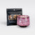 A  pink and black marbled teacup filled with wax and wick is next to a black resealable pouch of loose-leaf tea. Both items are labeled as “Almond Lemon Panna Cotta.”