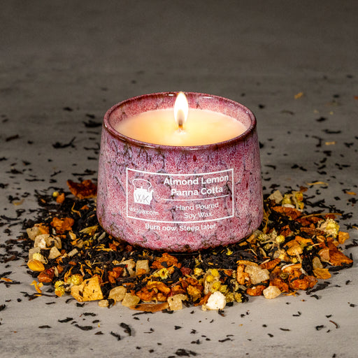 A lit candle in a textured blue and purple marbled ceramic tea cup, surrounded by a ring of black tea leaves, dried lemon peels, and other fruit inclusions