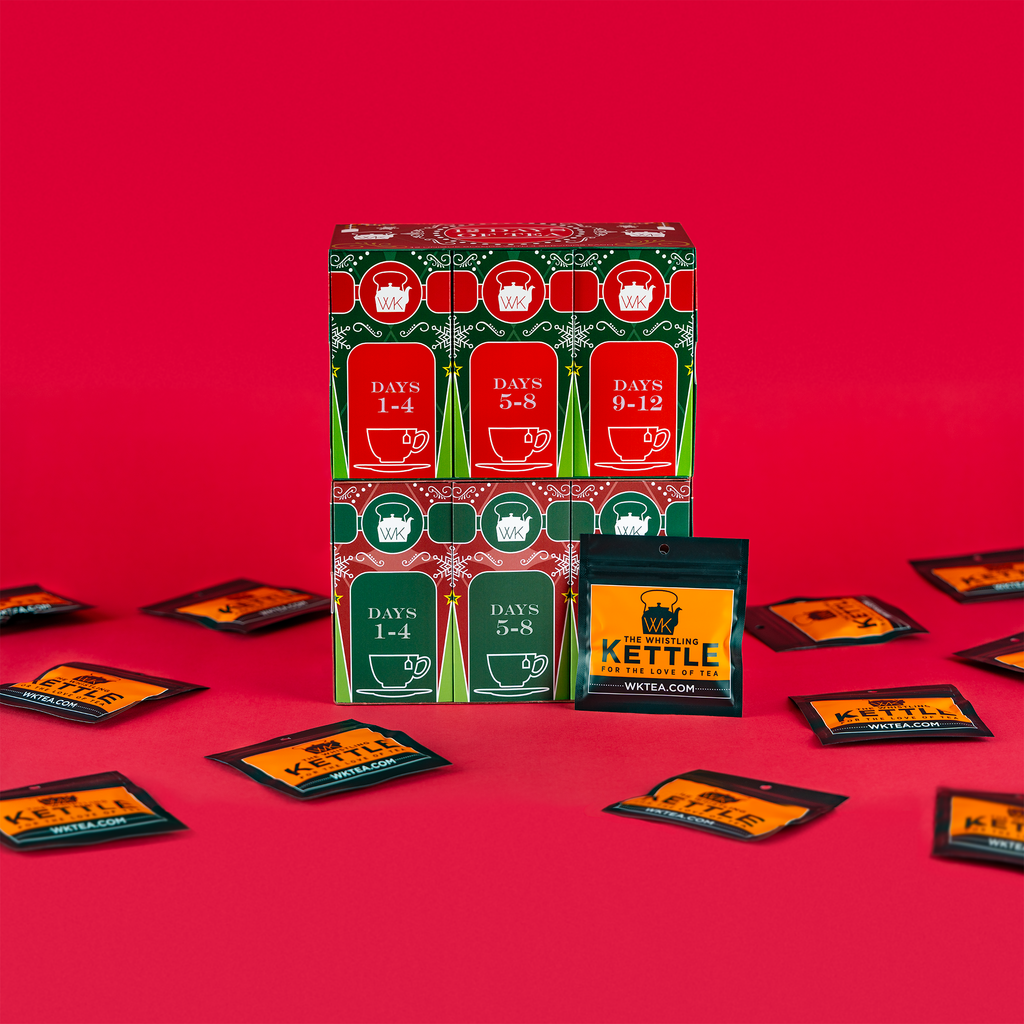 A 12 Days of Tea advent calendar stands open against a red background with individual tea packets displayed around the box