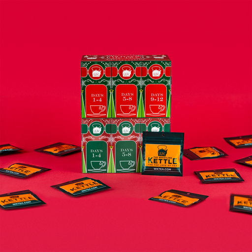 A 12 Days of Tea advent calendar stands open against a red background with individual tea packets displayed around the box