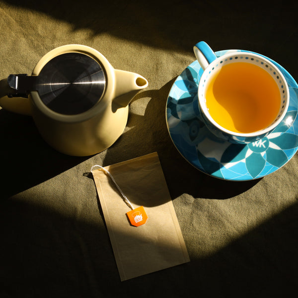 A cup of tea sits next to a tea pot