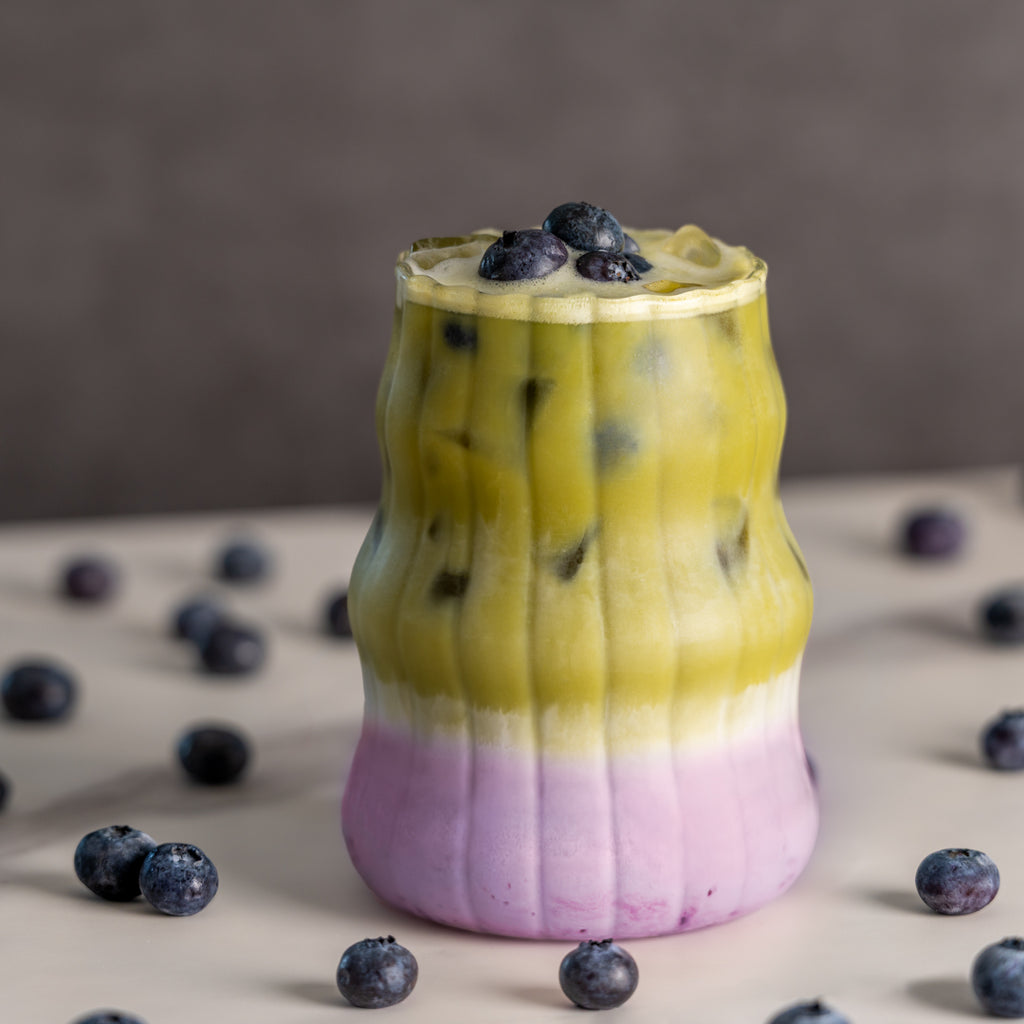 Blueberry matcha latte with a creamy purple blueberry layer, topped with blueberries and surrounded by fresh blueberries
