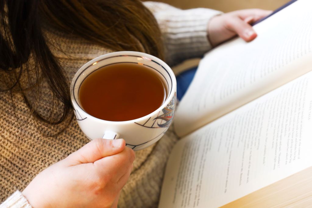 A woman holds a cup of tea while reading a book