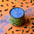 Butterfly Blue Matcha latte topped with blue foam, surrounded by dried butterfly pea flowers on an orange surface