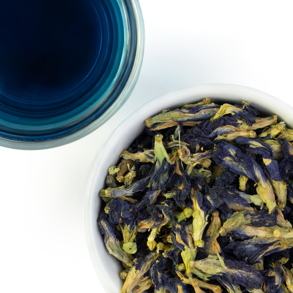 Overhead photo of whole Butterly Pea Flower alongside glass of a vivid blue tea.