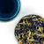 Overhead photo of whole Butterly Pea Flower alongside glass of a vivid blue tea.
