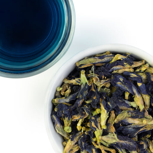 Overhead photo of whole Butterly Pea Flower alongside glass of a vivid blue tea.