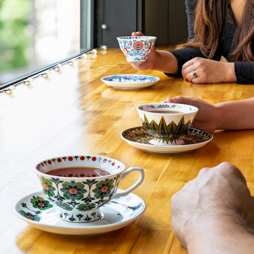 Dappled in sunlight and atop a wooden table, three distinct hands enjoy a cup of tea in each variation of the  Tea Cup and Saucer, Classic Edition collection