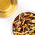 Close-up of a loose herbal tea blend with dried fruit and lemongrass beside a cup of golden tea