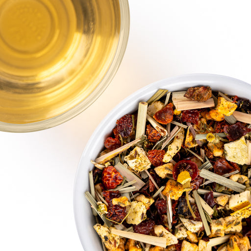 Close-up of a loose herbal tea blend with dried fruit and lemongrass beside a cup of golden tea