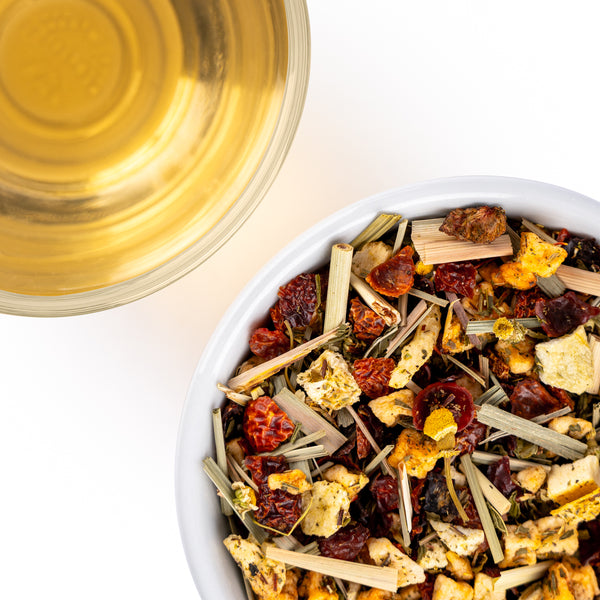Close-up of a loose herbal tea blend with dried fruit and lemongrass beside a cup of golden tea