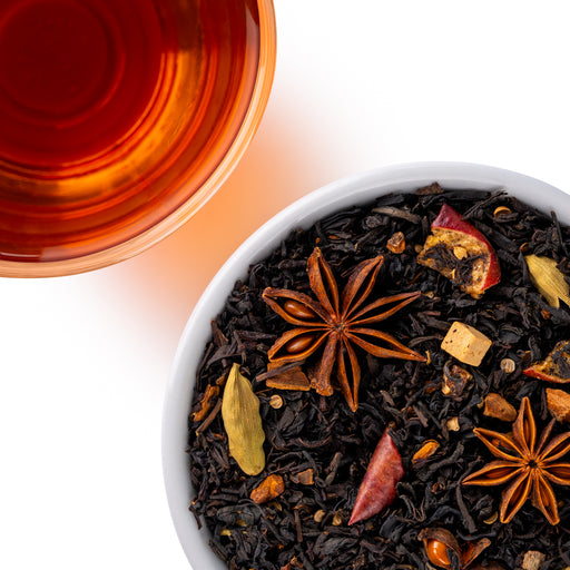 Overhead view of caramel apple chai loose-leaf tea with star anise, cardamom, cinnamon, apple pieces, and warm amber tea