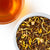 Overhead photo of Caramel Mate loose-leaf tea beside a warm brew cup of tea with an amber tone.