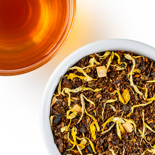 Overhead photo of Caramel Mate loose-leaf tea beside a warm brew cup of tea with an amber tone.