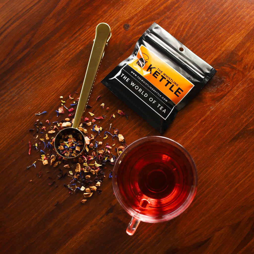 Glass of brewed Casablanca next to tea sample bag and Gold Tea Scoop filled with Casablanca loose leaf tea.