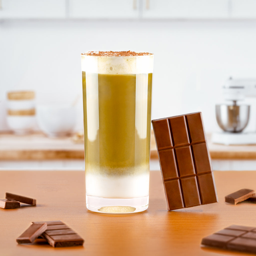 Iced chocolate matcha latte topped with cocoa powder beside dark chocolate bars
