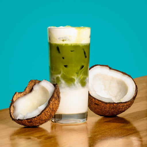 Iced coconut matcha latte with creamy coconut milk and coconut halves on a wooden table