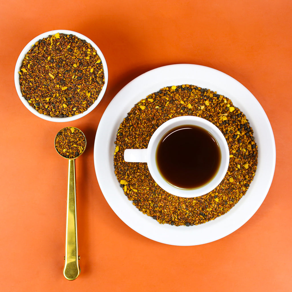 Cup of brewed Comfort Chaga on top of plate full of loose leaf Comfort Chaga tea.