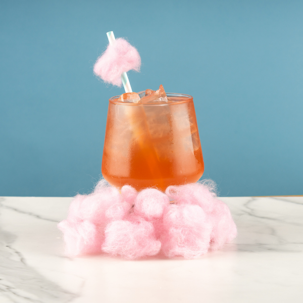 Pink cocktail drink with cotton candy garnish on a blue background.