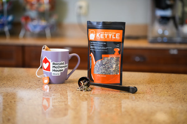 Purple mug with Ronald McDonald House branding, next to  a Whistling Kettle tea bag. 