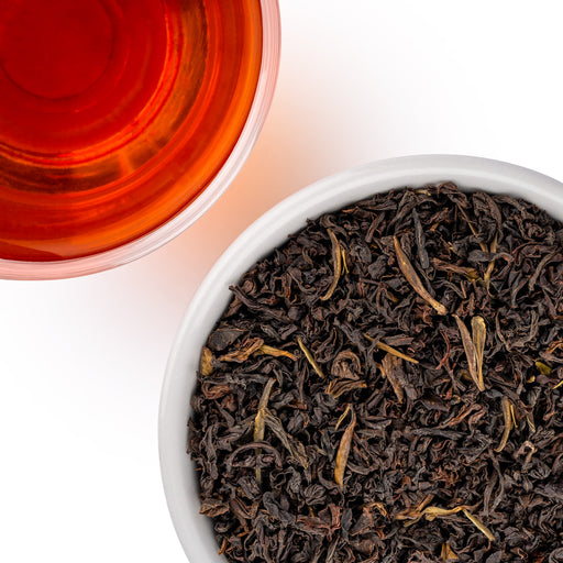 A top-down view showing a white bowl filled with dark loose-leaf tea and a glass of amber-red brewed tea on a white background