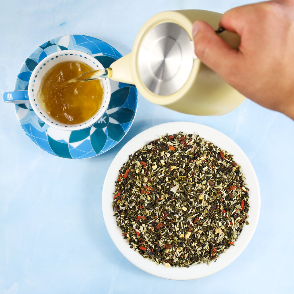 Pouring Feel Better tea into a tea saucer, plate of tea leaves sitting beside it.