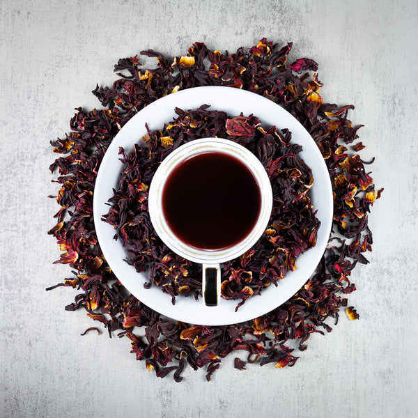 Cup of Hibiscus Bold Leaf tea in the middle of Hibiscus Bold Leaf loose leaf tea.