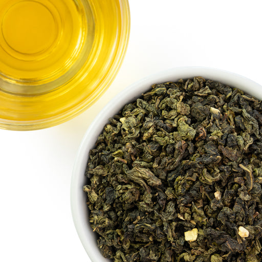 Dry imperial orange oolong tea leaves in a white bowl with a glass of brewed orange oolong tea on a white background