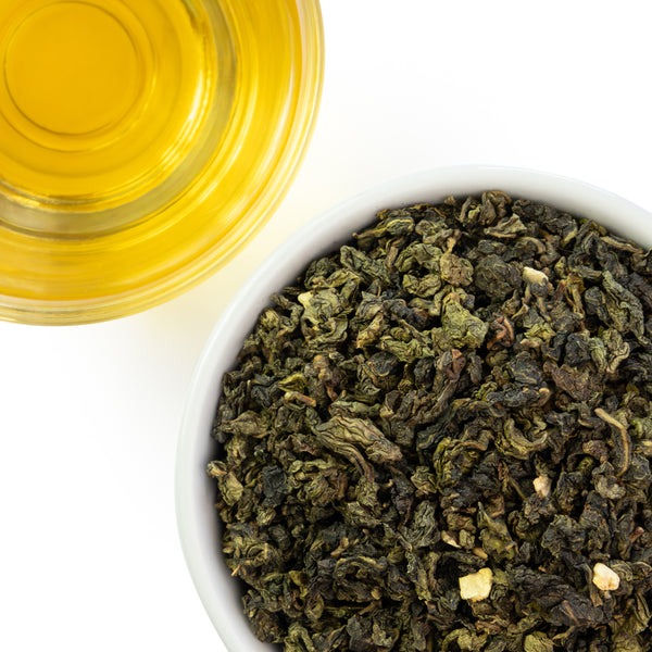 Dry imperial orange oolong tea leaves in a white bowl with a glass of brewed orange oolong tea on a white background