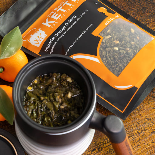 Mug with infuser steeping oolong tea leaves next to a 4oz size bag of Imperial Orange Oolong tea with oranges sitting next to the bag