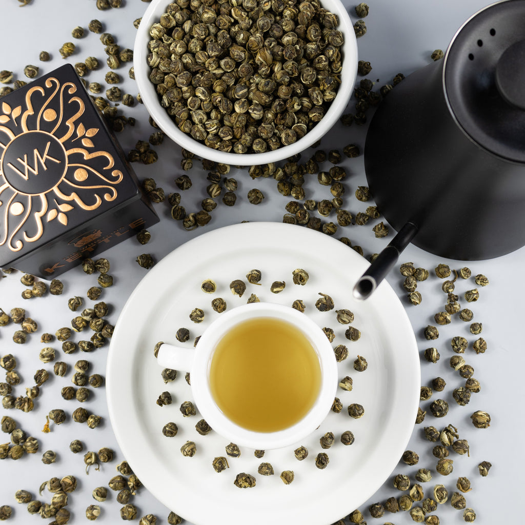 Cup of Jasmine Pearls tea surrounded by Jasmine Pearls loose leaf tea and other teware.