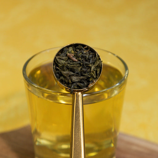 Glass of tea with a gold spoon holding tea leaves against a yellow background