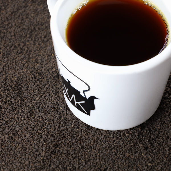 A white ceramic coffee mug filled with black coffee, resting on a bed of dark coffee grounds